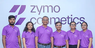 Group of six people wearing purple shirts standing in front of a Zymo Cosmetics logo.
